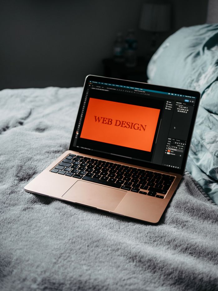 who-we-are A laptop on a bed showing web design software, creating a cozy workspace.